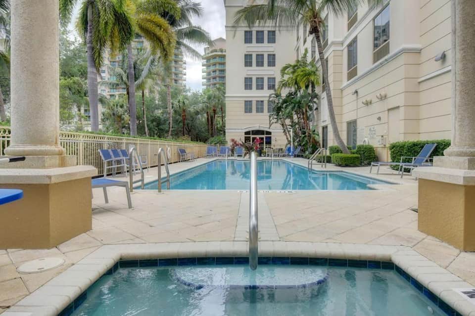Luxurious resort pool with spa jet in foreground, surrounded by tall palm trees and multi-story hotel buildings
