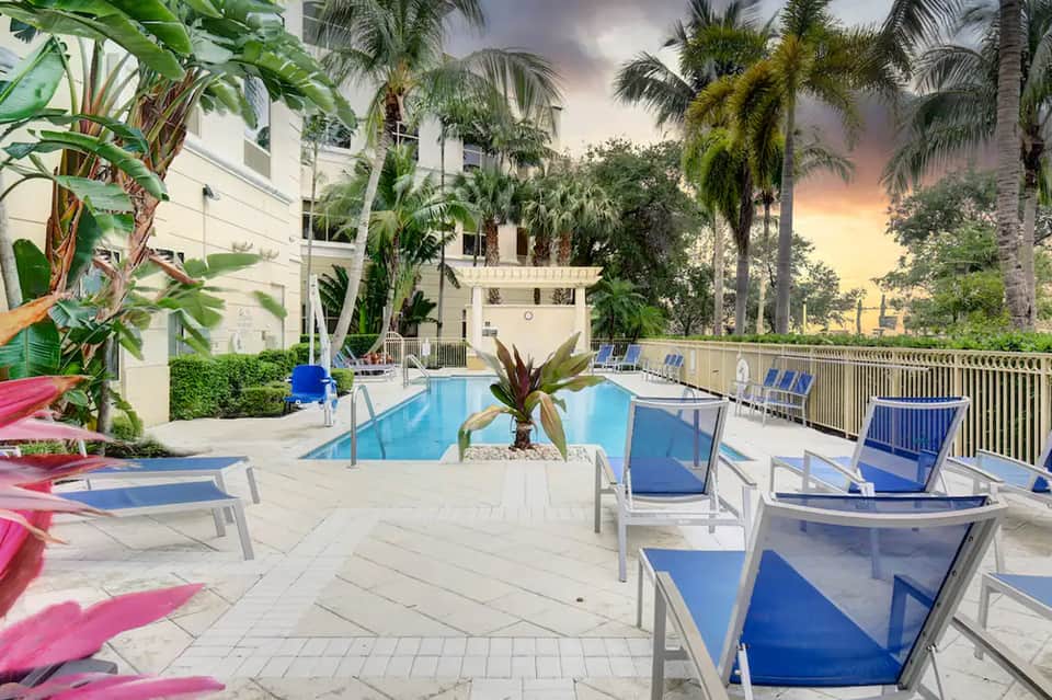 Resort pool area with palm trees, lounge chairs, and tropical landscaping at golden hour sunset