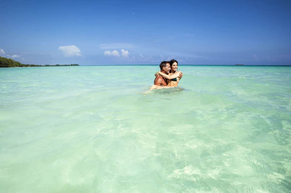 Couple embracing in shallow turquoise ocean water with clear sky and distant shore
