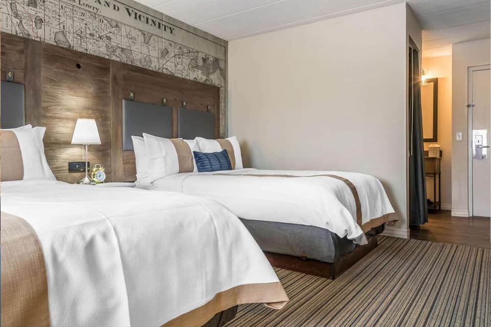 Modern hotel room with two queen beds, wood headboards, and striped carpet flooring