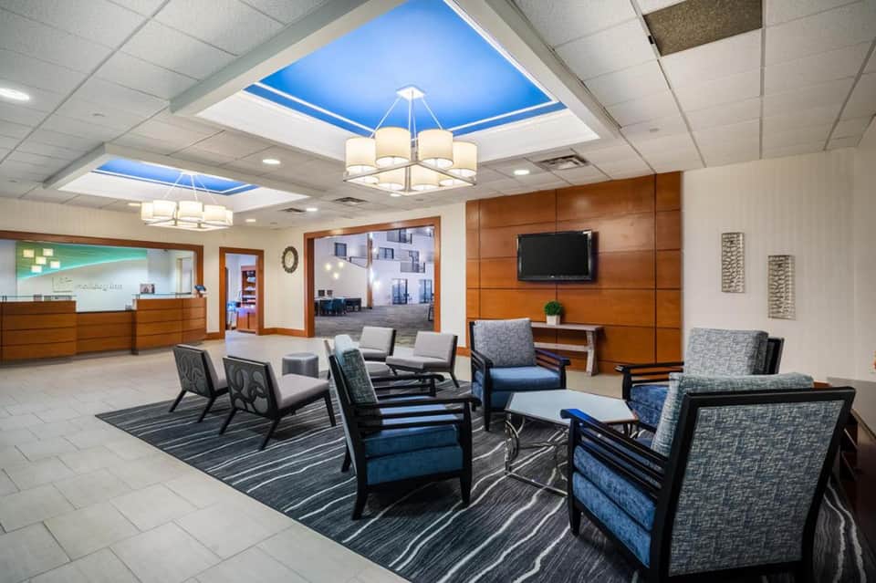 Modern hotel lobby with blue ceiling skylights, wood paneling, comfortable seating, and reception desk