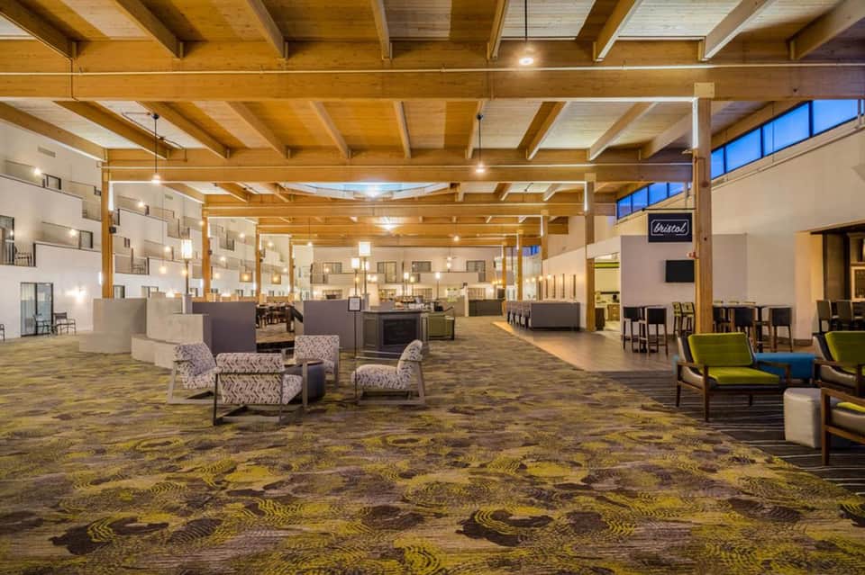Modern hotel lobby with wooden beam ceiling, seating areas, and patterned carpet flooring