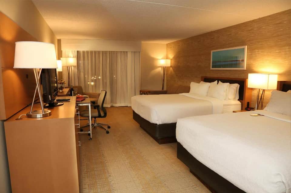 Hotel room with two queen beds, work desk, warm lighting, and patterned wallpaper