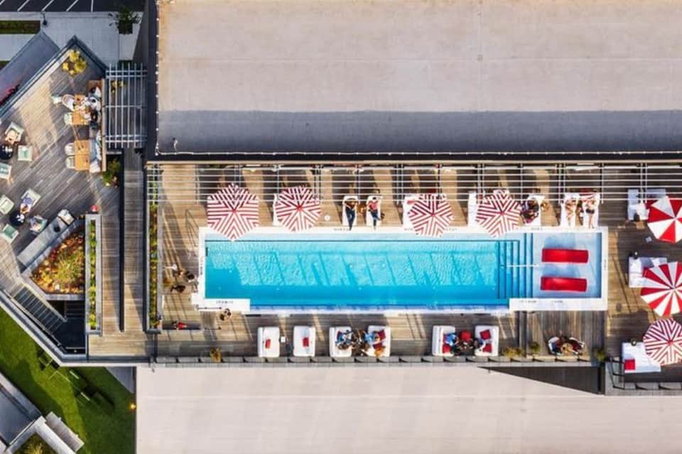 Aerial view of modern rooftop pool with red and white umbrellas and surrounding deck