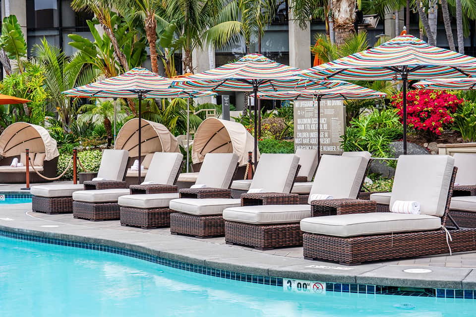 Poolside lounge area with striped umbrellas, wicker recliners, and tropical landscaping