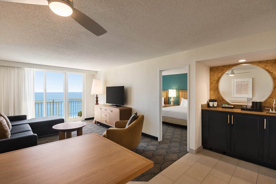 Hotel suite with ocean view balcony, living area, bedroom, and contemporary furnishings