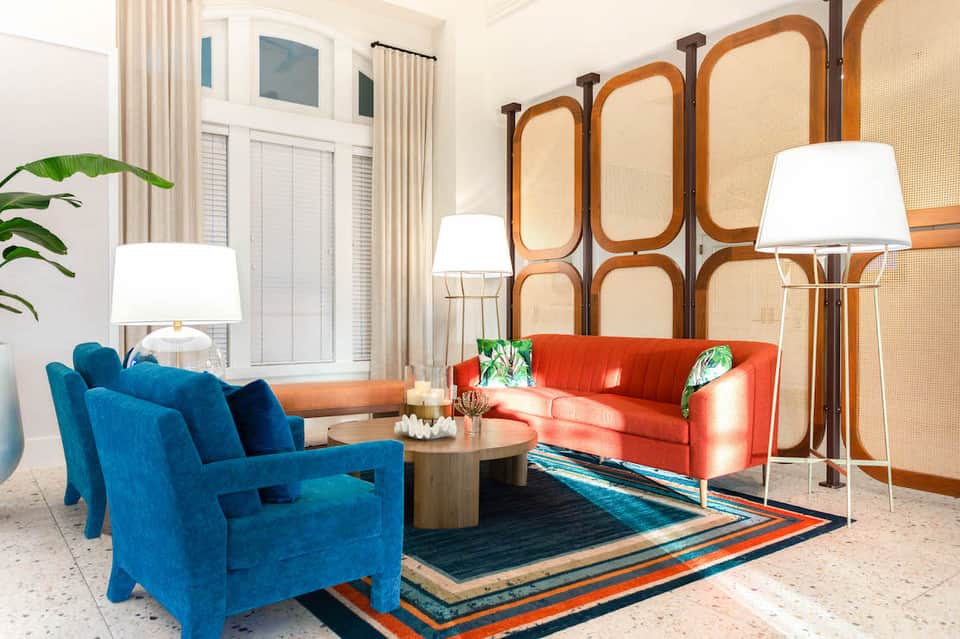 Luxury living room with blue armchair, coral sofa, wooden room divider, and colorful rug