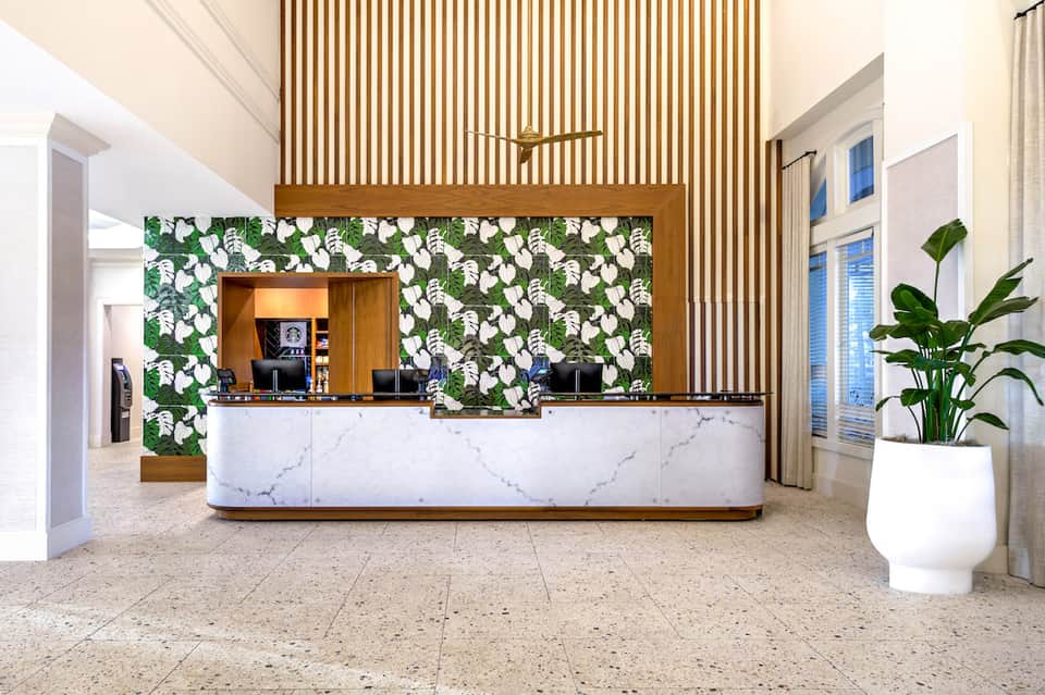 Contemporary hotel reception desk with tropical leaf wallpaper, marble counter, and wooden slat backdrop