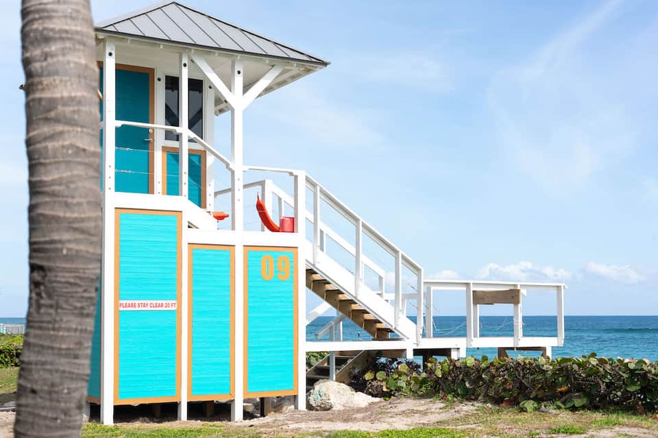 Colorful lifeguard tower with turquoise and orange trim on sandy beach near palm tree