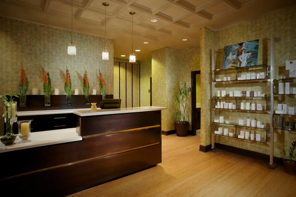 Upscale spa reception desk with dark wood finishes, green wallpaper, and shelved product display
