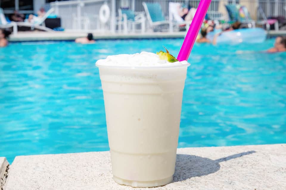 Frozen cocktail with whipped cream and pink straw by resort pool with swimmers