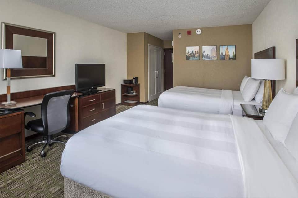 Modern hotel room with two queen beds, work desk, TV, and contemporary furnishings