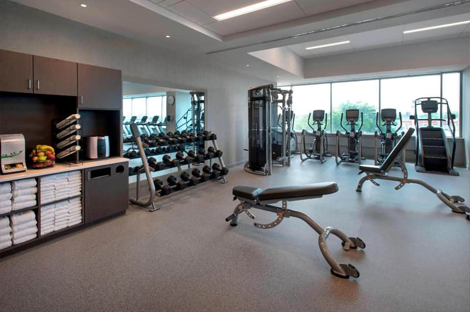 Modern fitness center with cardio equipment, weight racks, dumbbells, and large windows overlooking landscape