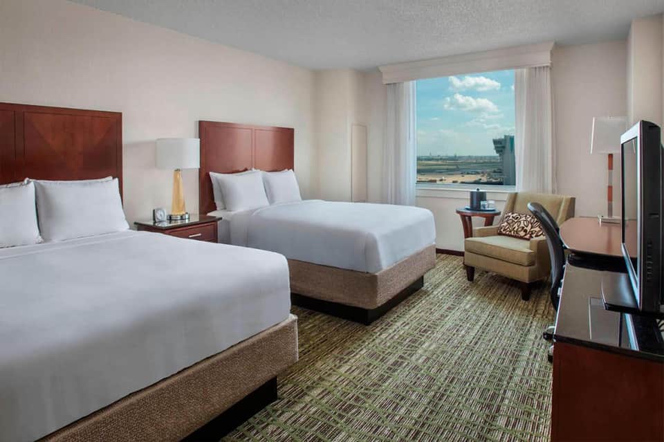 Hotel room with two queen beds, burgundy headboards, and panoramic window overlooking landscape