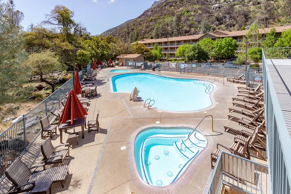 Resort pool area with two turquoise pools, lounge chairs, red umbrellas, and mountain backdrop