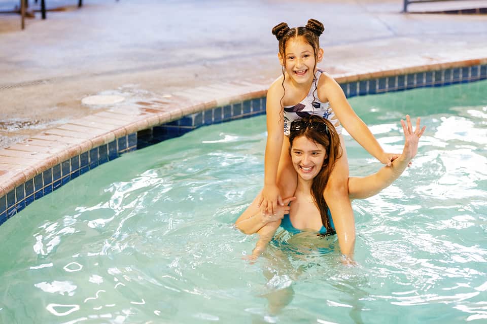 Two young girls smiling in a shallow indoor pool with green water