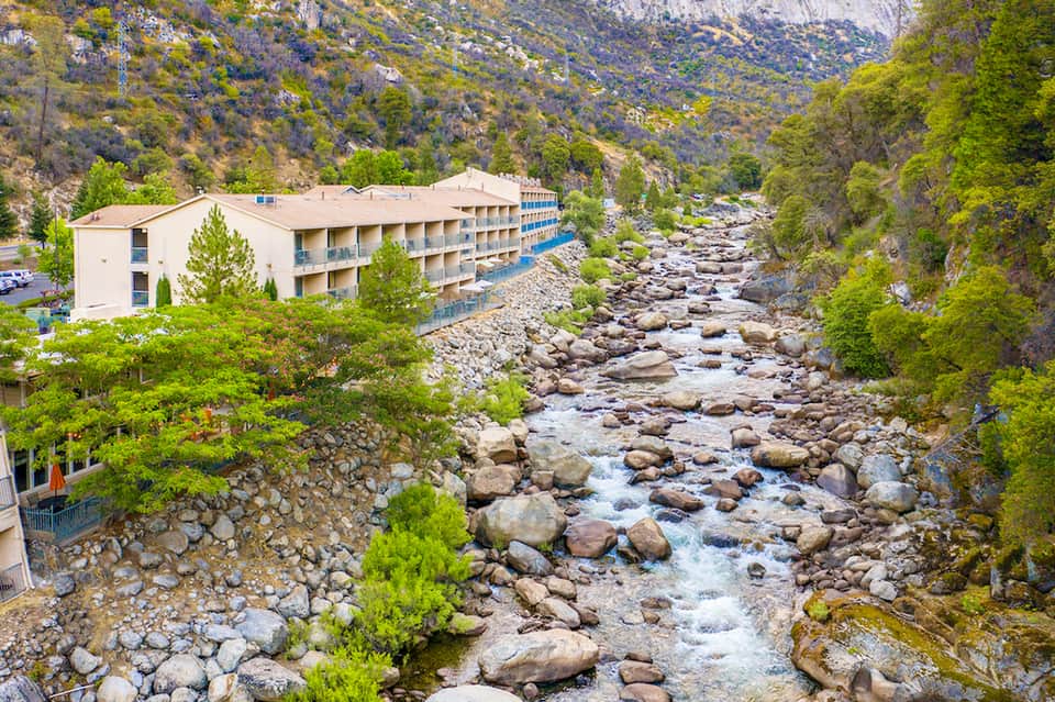 Riverside hotel nestled in mountain valley with rocky stream and forested landscape