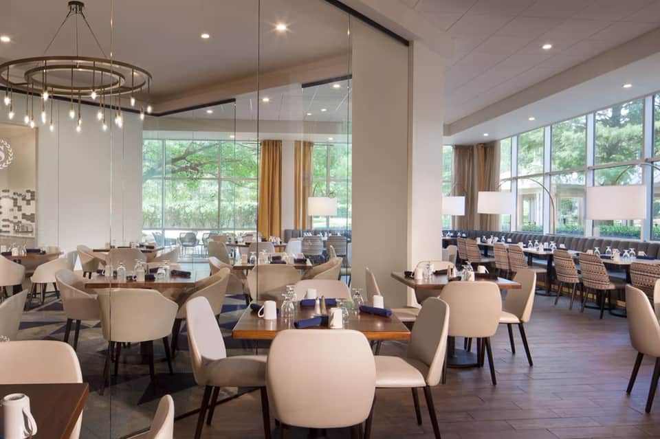 Contemporary hotel restaurant with round tables, pendant lighting, and floor-to-ceiling windows