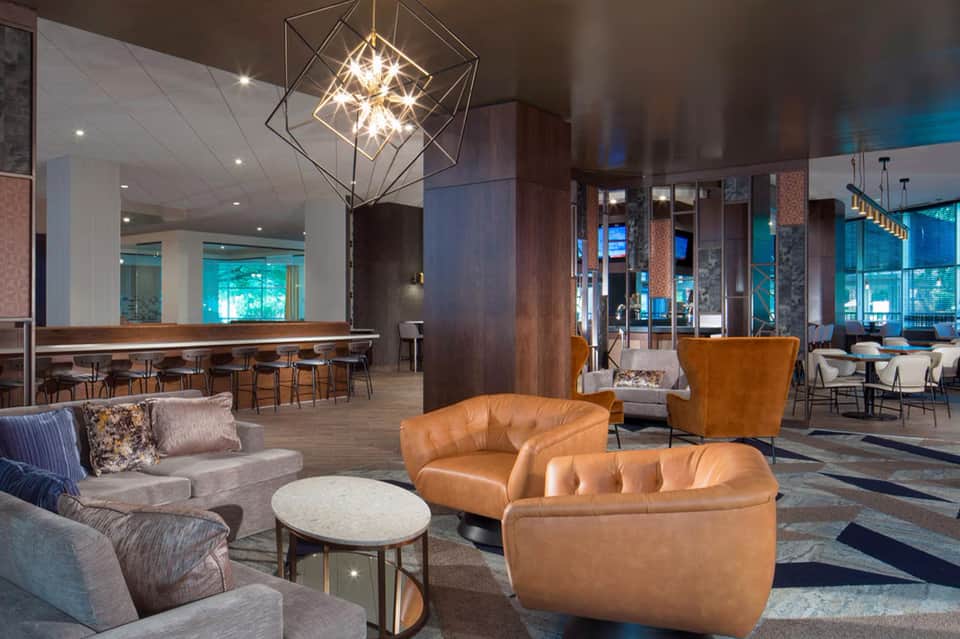 Modern hotel lobby with tan leather chairs, geometric chandelier, and contemporary furnishings around a round table