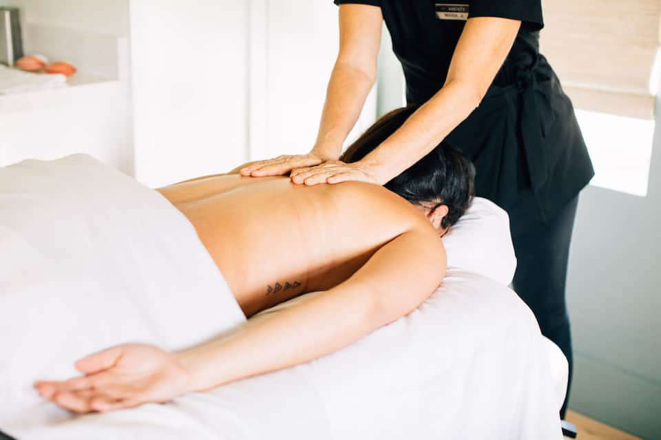 Massage therapist performing deep tissue massage on client's back in spa treatment room