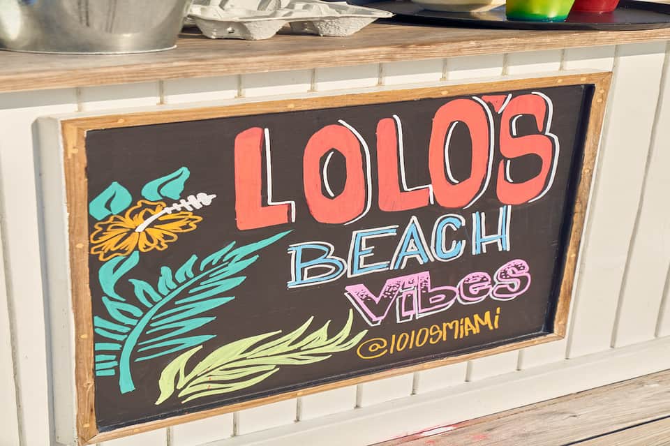 Chalkboard sign reading 'Lolos Beach Vibes' with colorful tropical leaf designs