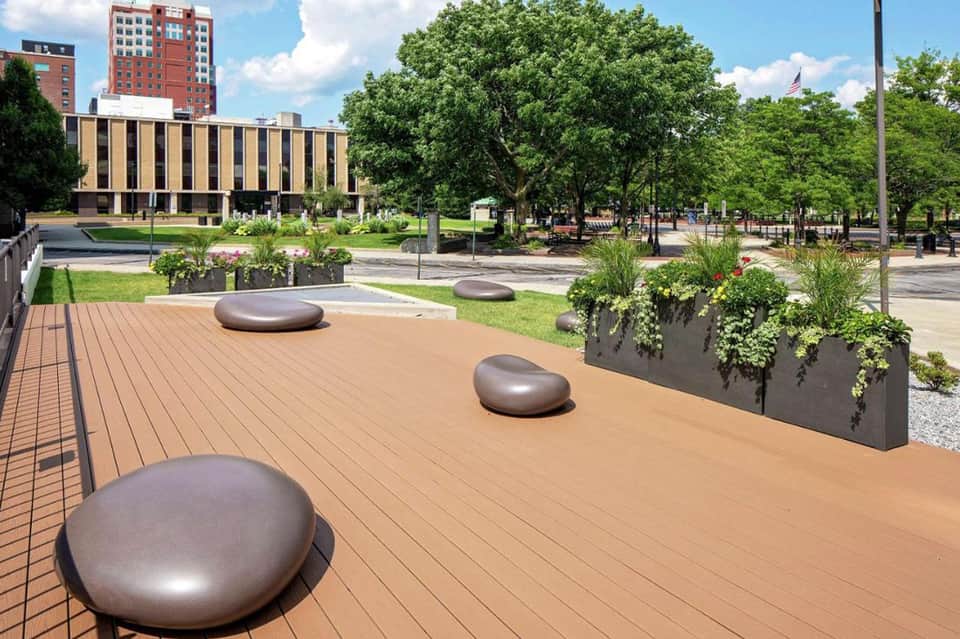 Urban rooftop terrace with metallic seating pods, planter boxes, and city park views