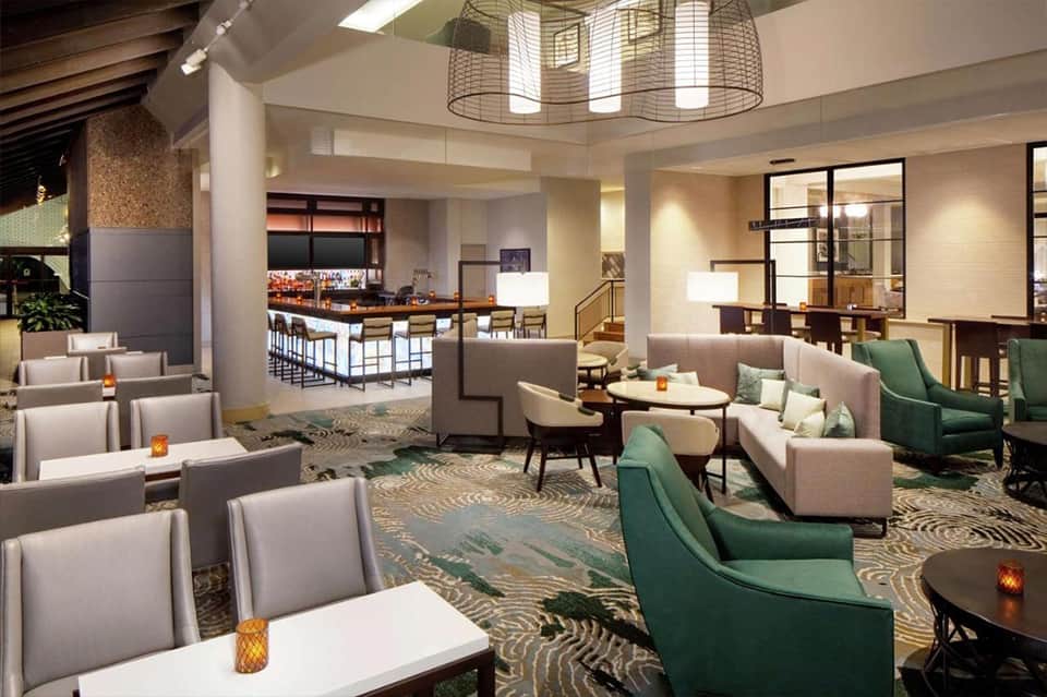 Hotel lobby lounge with green and beige seating, decorative lighting, bar area, and patterned carpeting