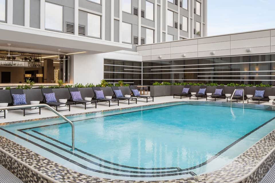 Modern hotel pool deck with lounge chairs, purple cushions, and high-rise building backdrop