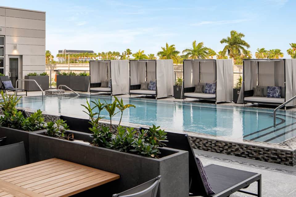 Rooftop pool deck with cabanas, lounge chairs, palm trees, and city skyline views