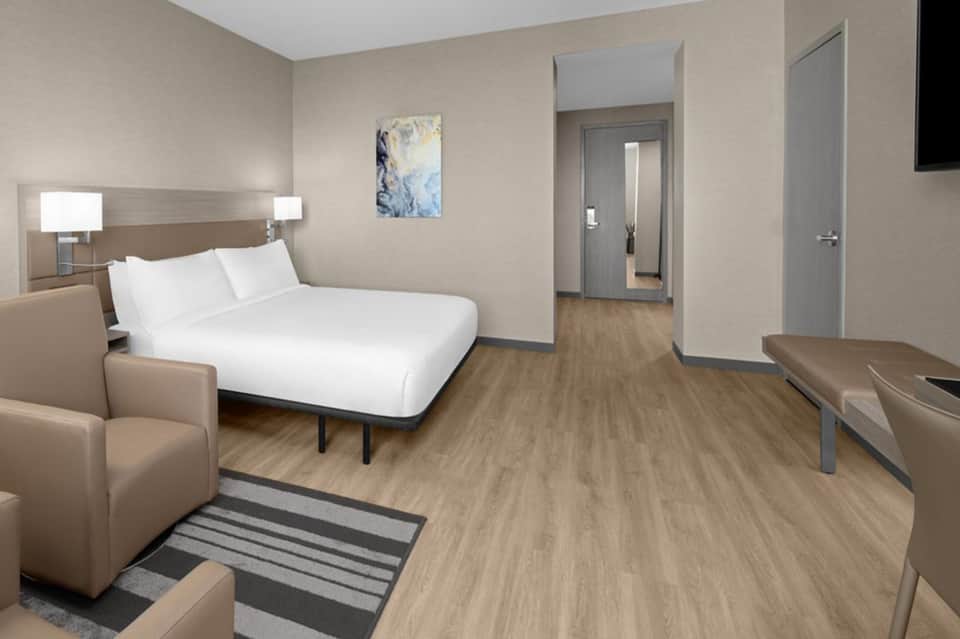 Contemporary hotel bedroom with queen bed, wood flooring, neutral tones, and ensuite bathroom