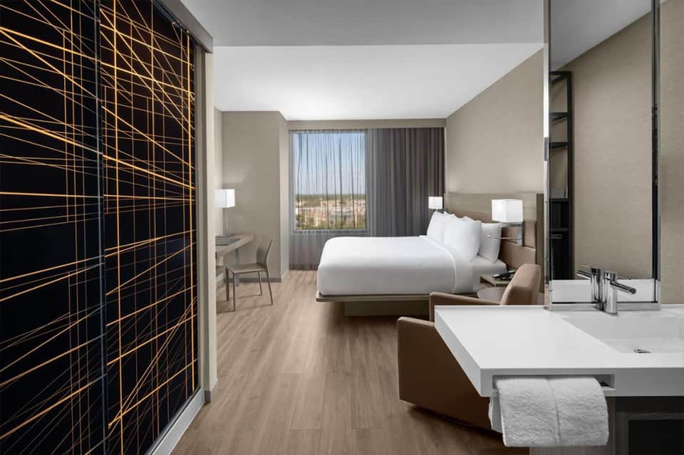 Modern hotel bedroom with geometric wall art, white bedding, and floor-to-ceiling windows with city view
