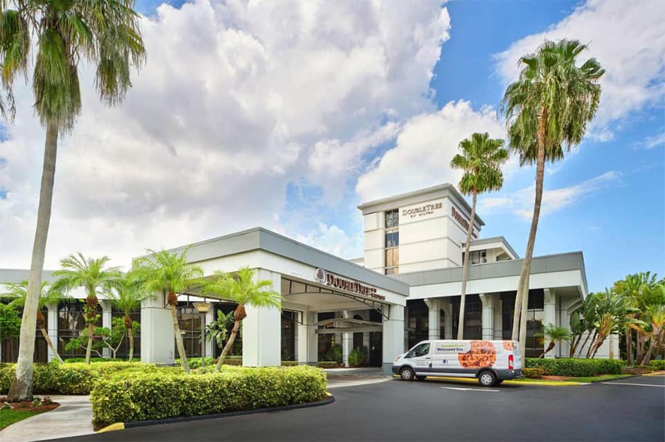 Modern hotel exterior with white architecture, palm trees, and covered entrance with service van