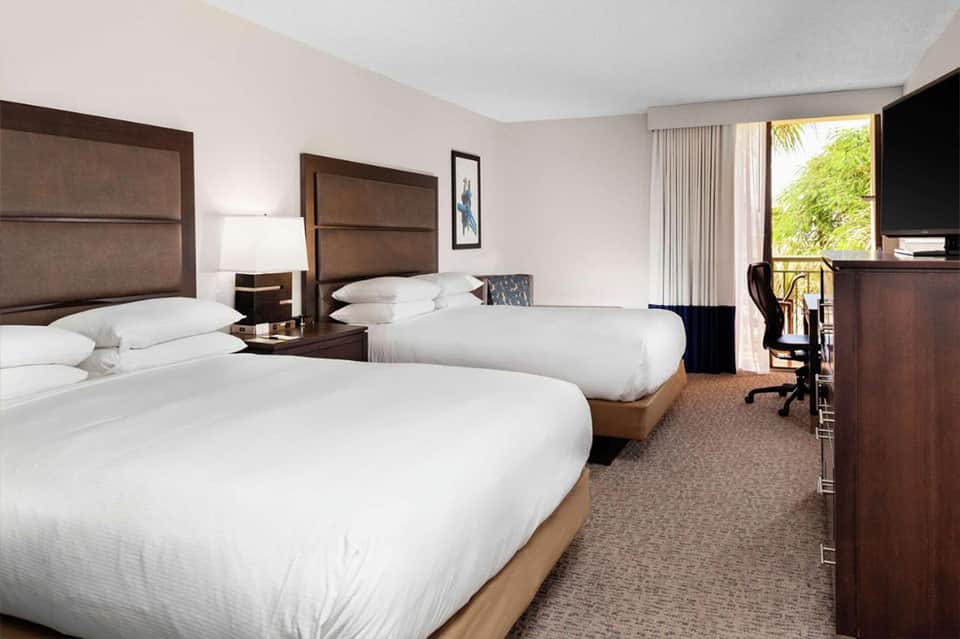 Hotel room with two queen beds, wooden headboards, and balcony overlooking tropical landscape