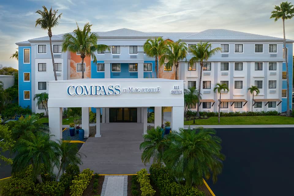 Compass by Margaritaville all-suites hotel exterior with blue and white facade and palm trees