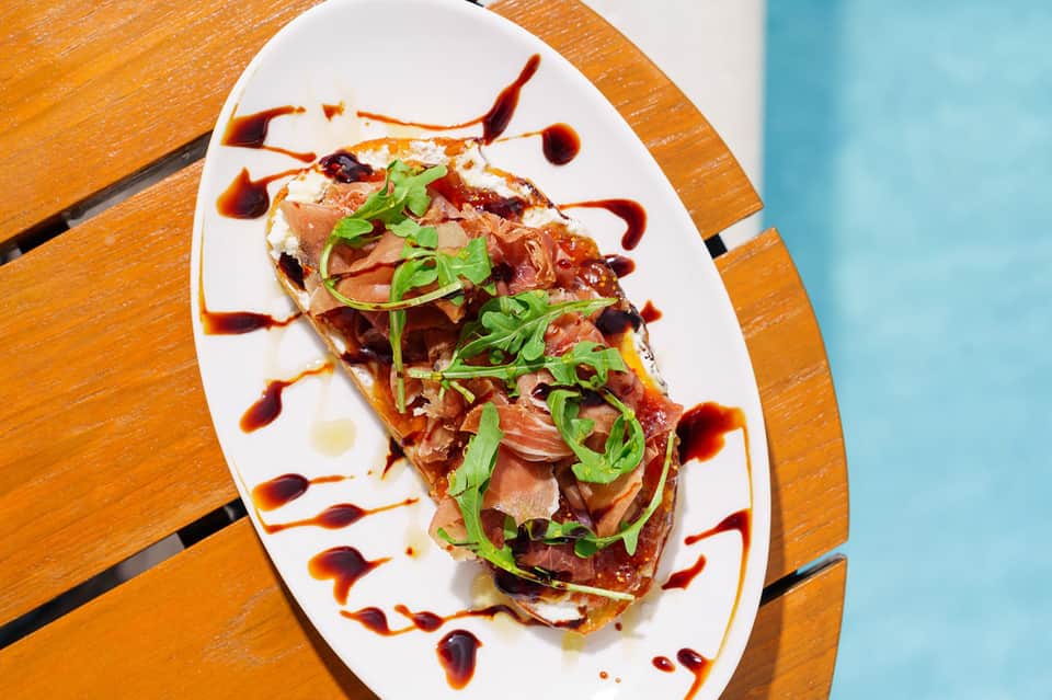 Gourmet plated dish with seared protein, greens, and decorative sauce on wooden table