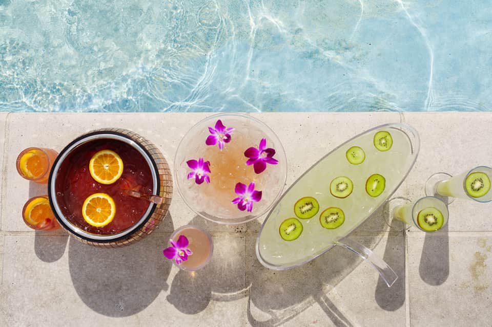 Overhead view of poolside beverages with fruit garnishes and flowers