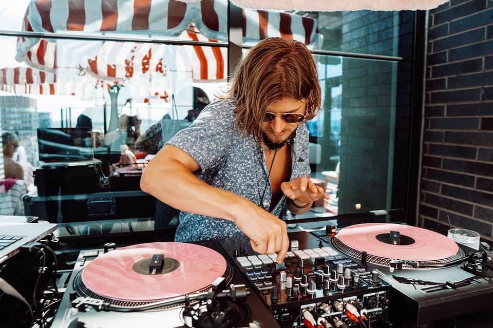 DJ performing with pink vinyl records at an elevated turntable with city view in background