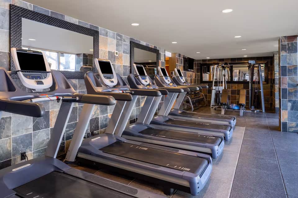 Modern fitness center with cardboard treadmills, mirrored walls, and stone tile flooring