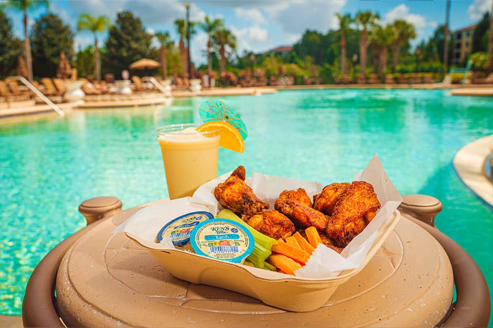 Poolside lunch float with fried chicken, fries, cheese, juice and orange slice garnish overlooking turquoise pool
