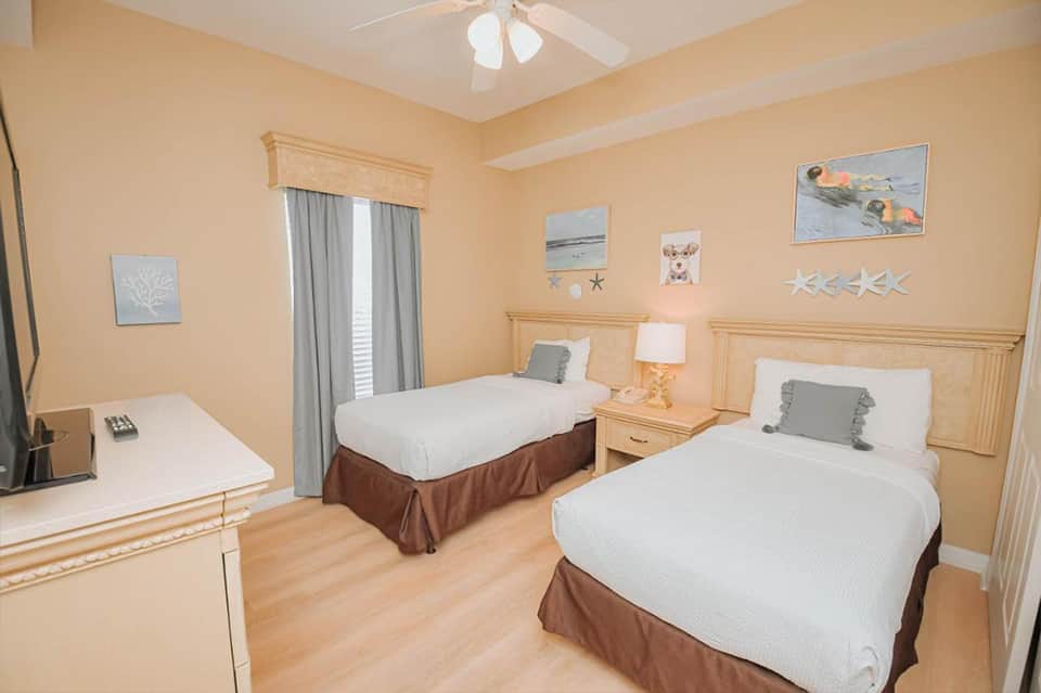 Bright beige hotel bedroom with two twin beds, wooden furniture, and nautical wall decorations
