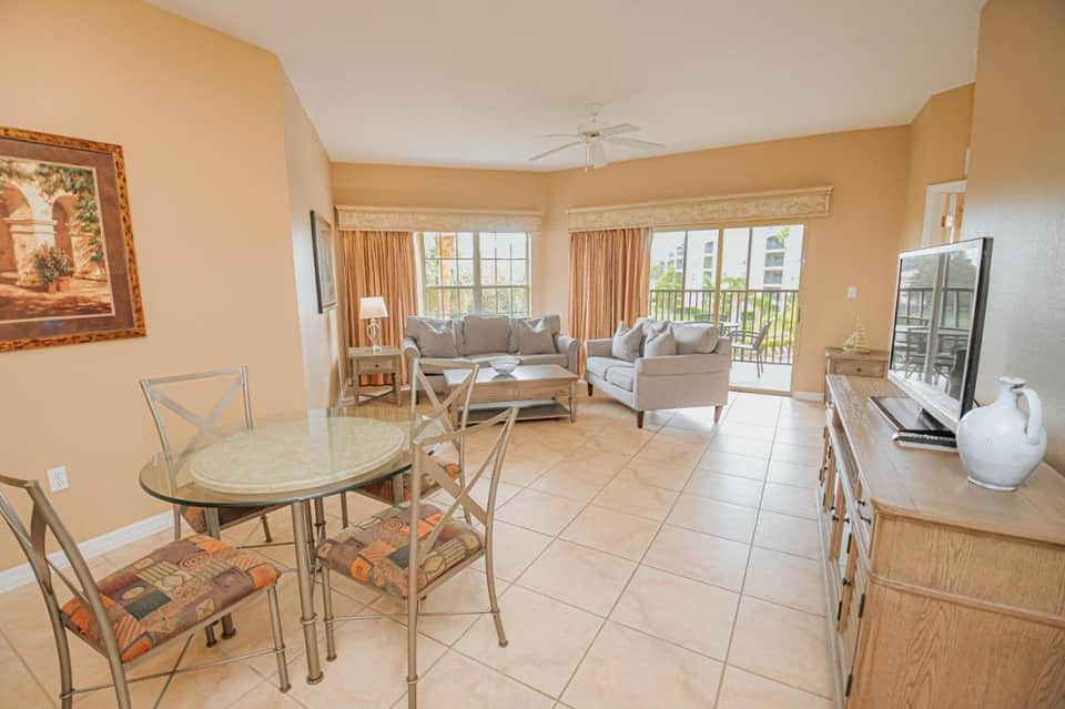 Spacious resort living room with peach walls, beige furnishings, dining table, and balcony overlooking grounds