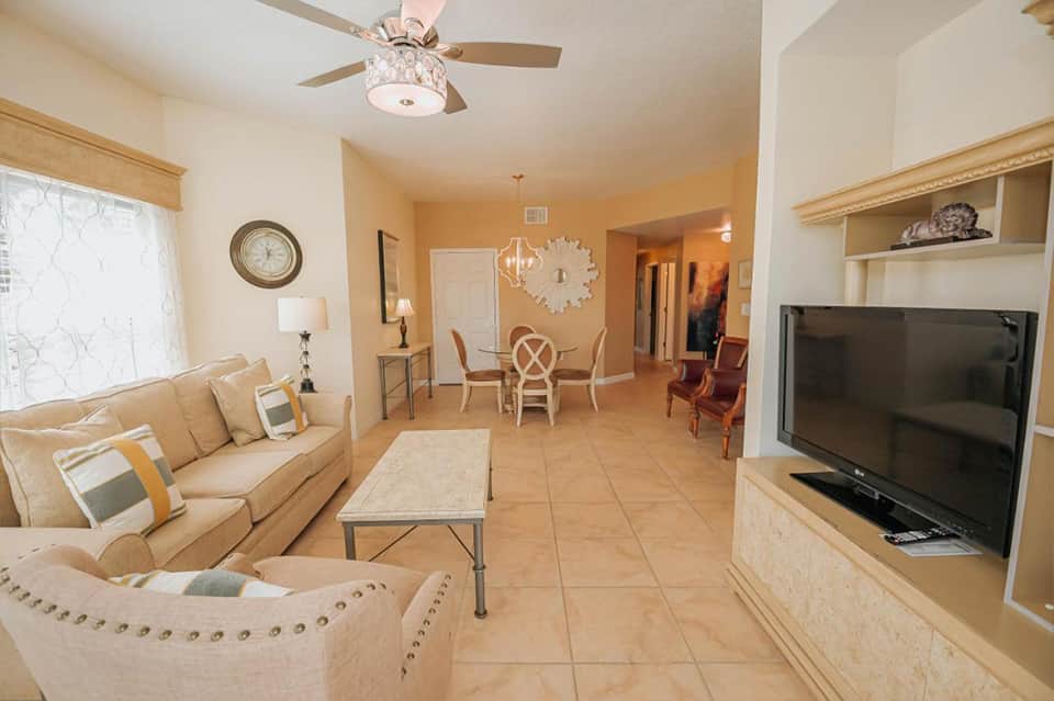 Spacious hotel suite with beige furnishings, ceiling fan, dining area, and entertainment center
