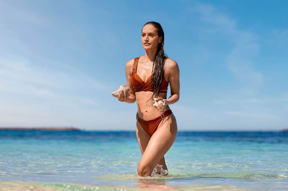 Woman in rust-colored bikini running into clear blue ocean water on a sunny beach day