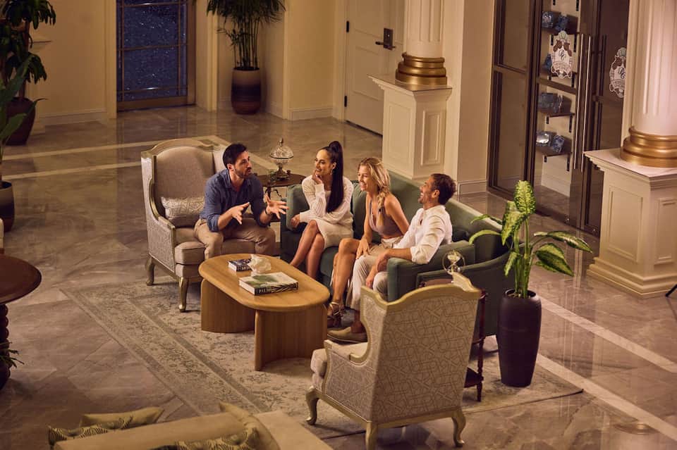 Elegant hotel lobby with guests conversing in seating areas surrounded by classical columns and marble flooring