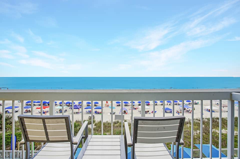 Beachfront view from deck with lounge chairs overlooking sandy beach and ocean