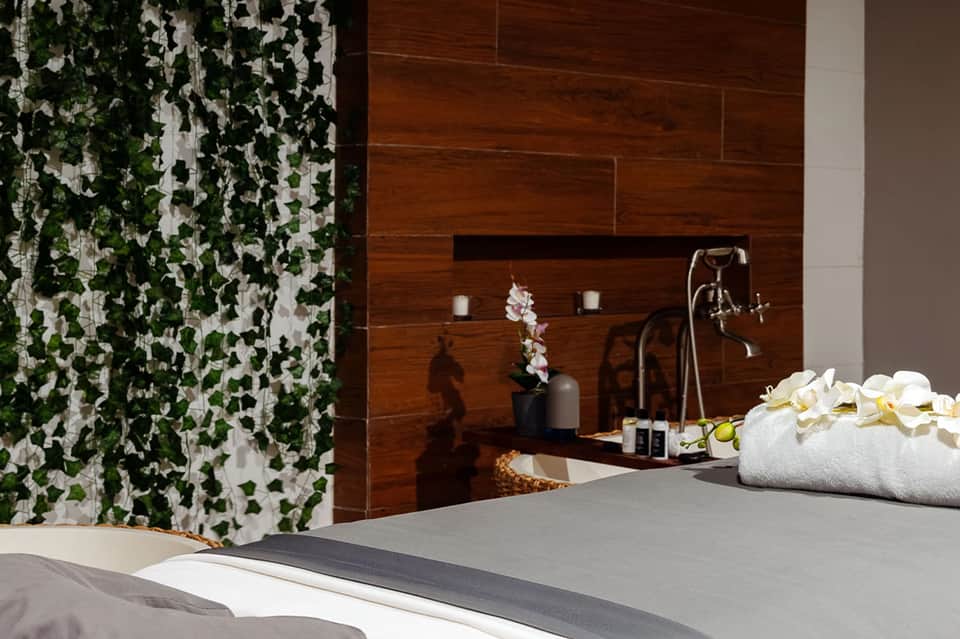 Luxury spa bathroom with wood-paneled walls, soaking tub, rainfall showerhead, white towels, and orchid flowers