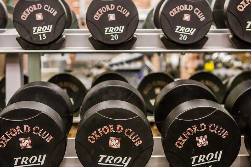 Black dumbbells labeled Oxford Club Troy on weight rack in fitness facility