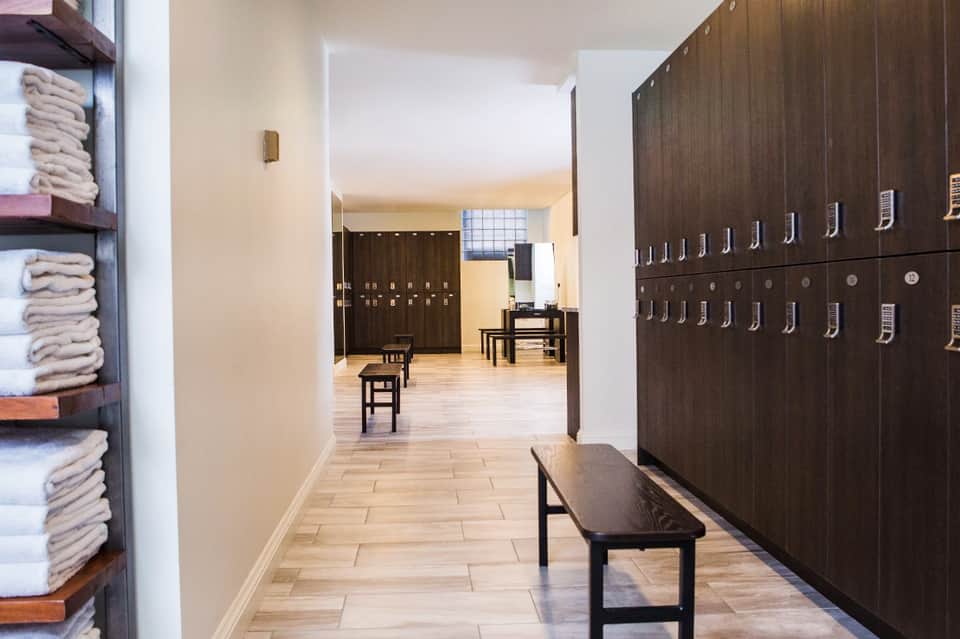 Spa locker room with dark wooden lockers, folded towels on shelves, and wooden benches in hallway