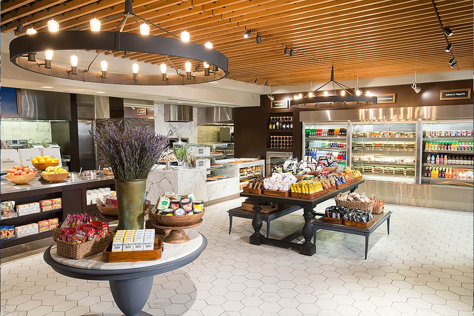 Modern hotel convenience store with bright lighting, fresh produce, refrigerated beverages, and snack displays