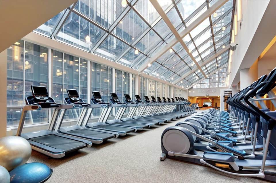 High-rise gym with rows of treadmills and exercise bikes facing floor-to-ceiling windows